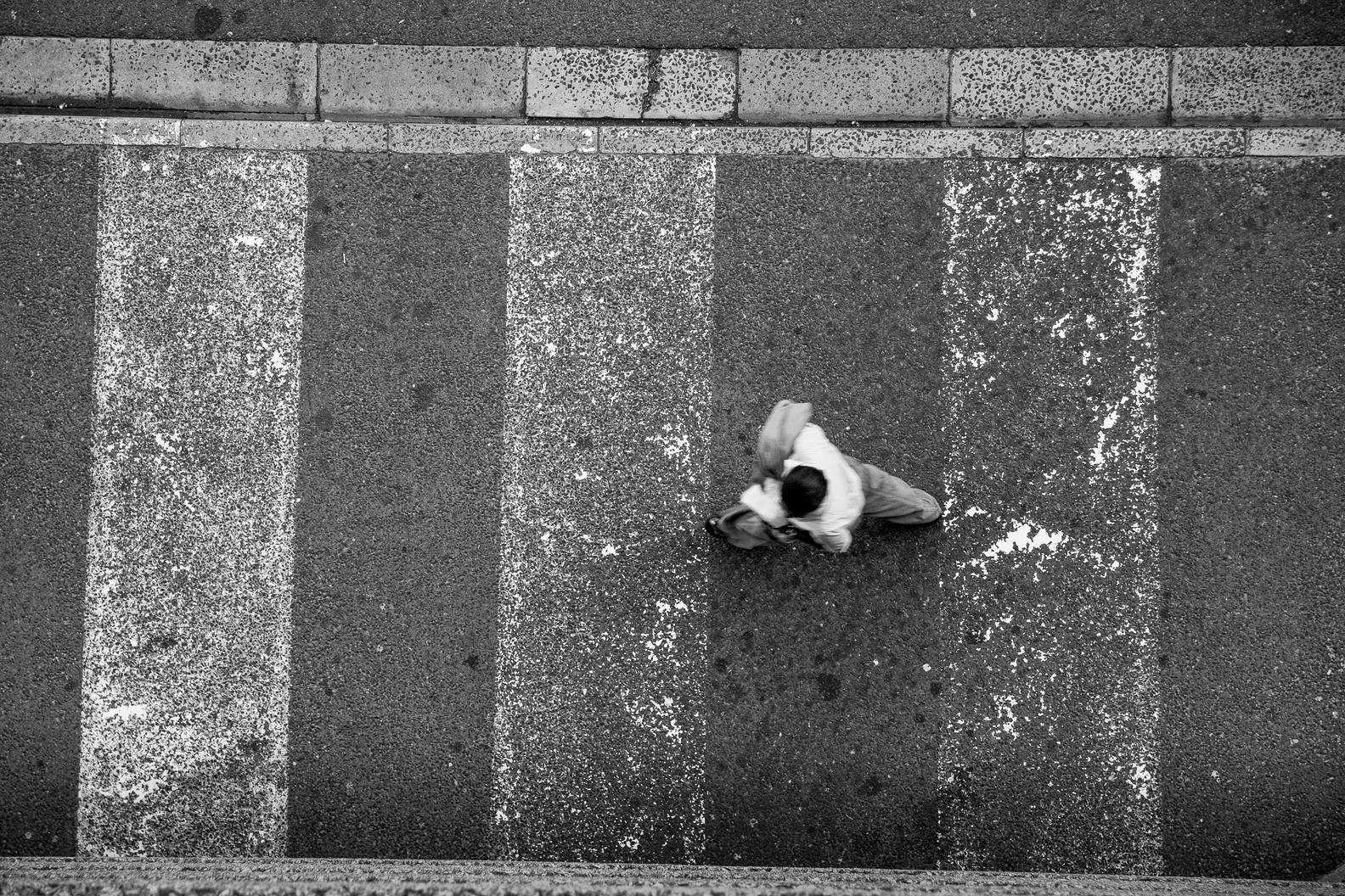 Looking straight down at a pedestrian crossing, with a single person walking across the painted white bars.
